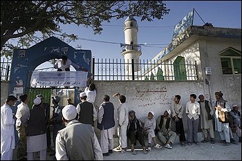 Afghan voters line up to cast their ballots as an Afghan election official hangs an election information banner over the entrance of a mosque made into a polling station in Kabul on Thursday Aug. 20, 2009. (AP Photo/David Guttenfelder)